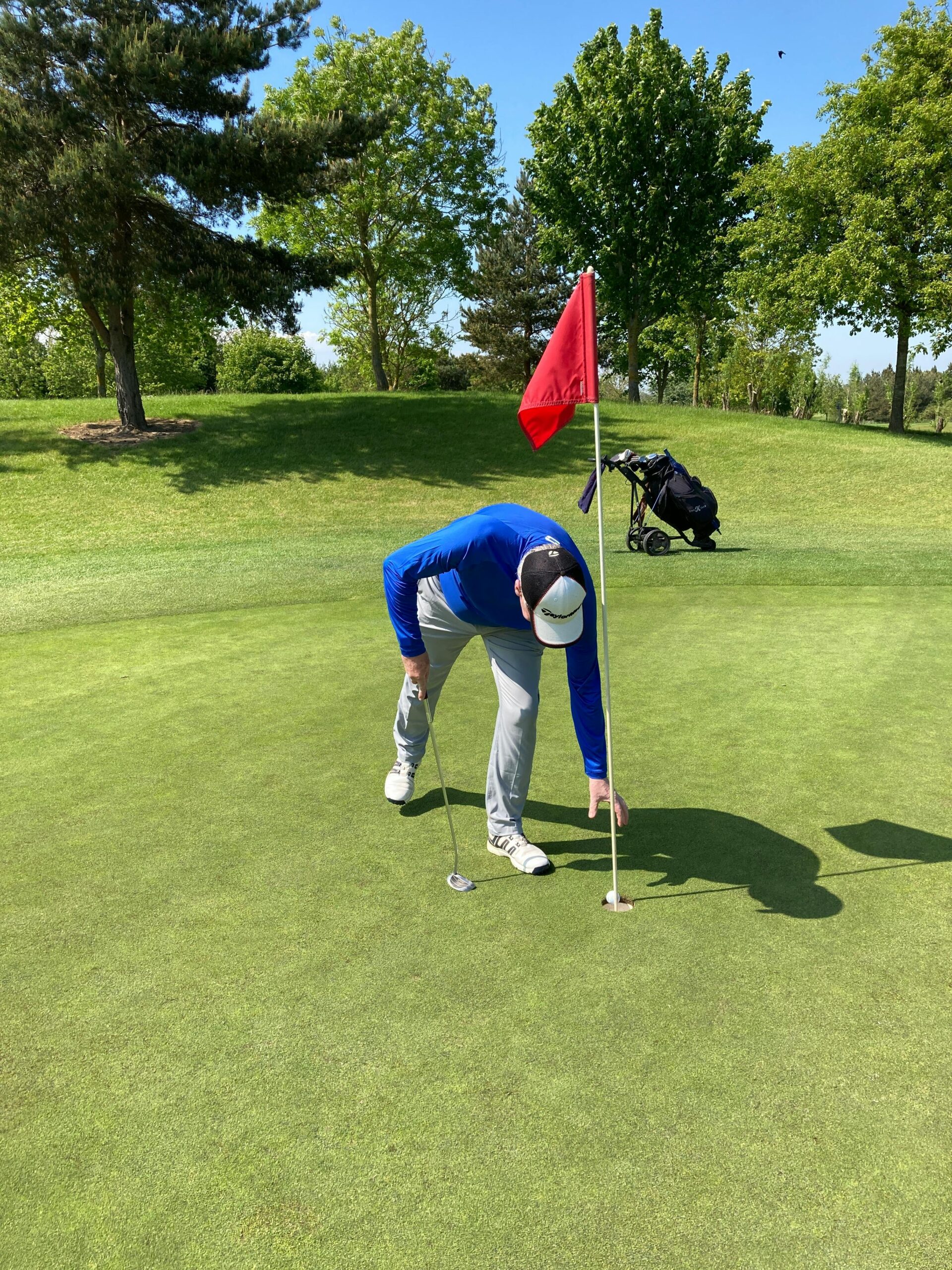 A golfer retrieves a golf ball from the hole on a green course. Sunny day, clear skies.